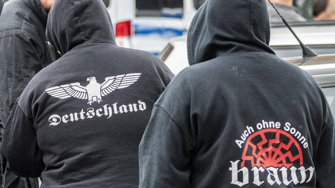 Man sieht von hinten mehrere Menschen, die Kapuzenpullis mit rechten Slogans tragen.