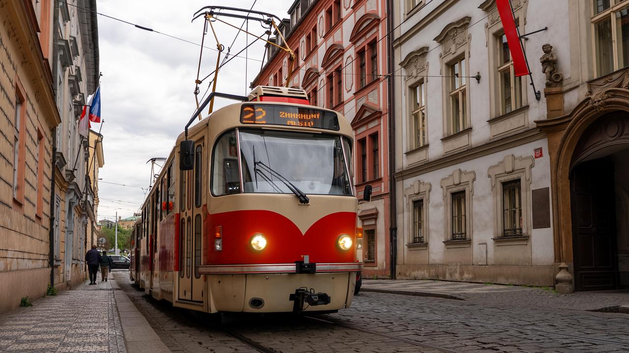 Eine älteres rot-beiges Straßenbahnmodell der Tramlinie 22 fährt in Prag in einer Straße mit Kopfsteinpflaster.