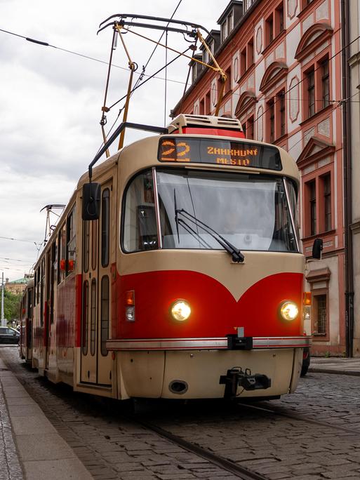 Eine älteres rot-beiges Straßenbahnmodell der Tramlinie 22 fährt in Prag in einer Straße mit Kopfsteinpflaster. Eine älteres rot-beiges Straßenbahnmodell der Tramlinie 22 fährt in Prag in einer Straße mit Kopfsteinpflaster.