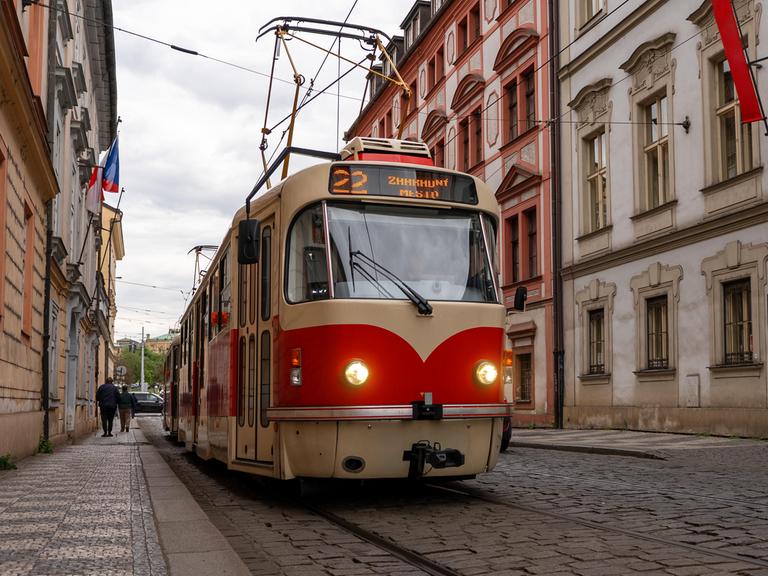 Eine älteres rot-beiges Straßenbahnmodell der Tramlinie 22 fährt in Prag in einer Straße mit Kopfsteinpflaster. Eine älteres rot-beiges Straßenbahnmodell der Tramlinie 22 fährt in Prag in einer Straße mit Kopfsteinpflaster.