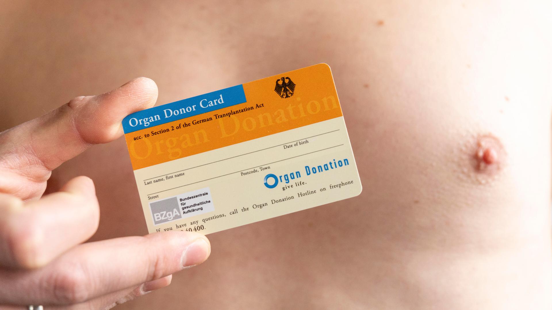 Ein Mann mit freiem Oberkörper hält einen Organspendeausweis in der Hand.