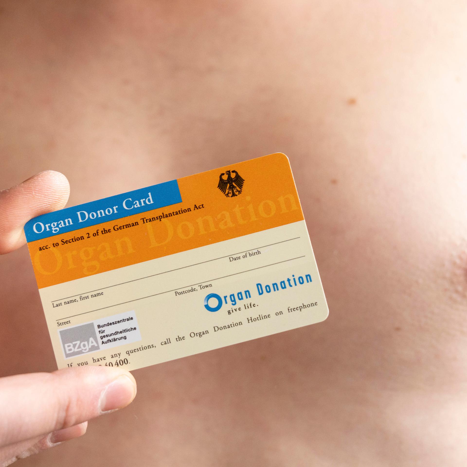 Ein Mann mit freiem Oberkörper hält einen Organspendeausweis in der Hand.