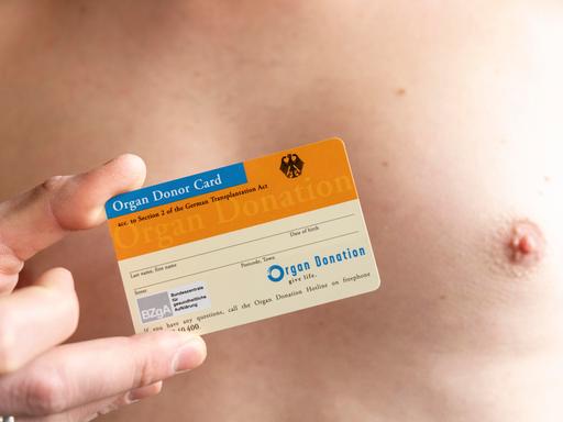 Ein Mann mit freiem Oberkörper hält einen Organspendeausweis in der Hand.