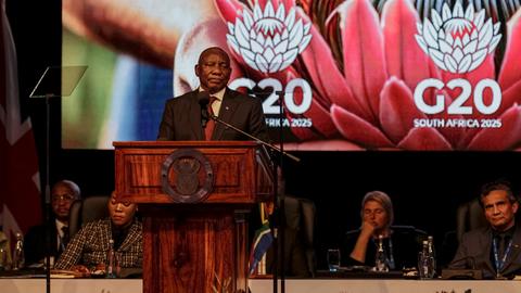 Ramaphosa steht an einem Rednerpult. Hinter ihm ist ein großer Bildschirm mit zwei Logos des Gipfels zu sehen. 