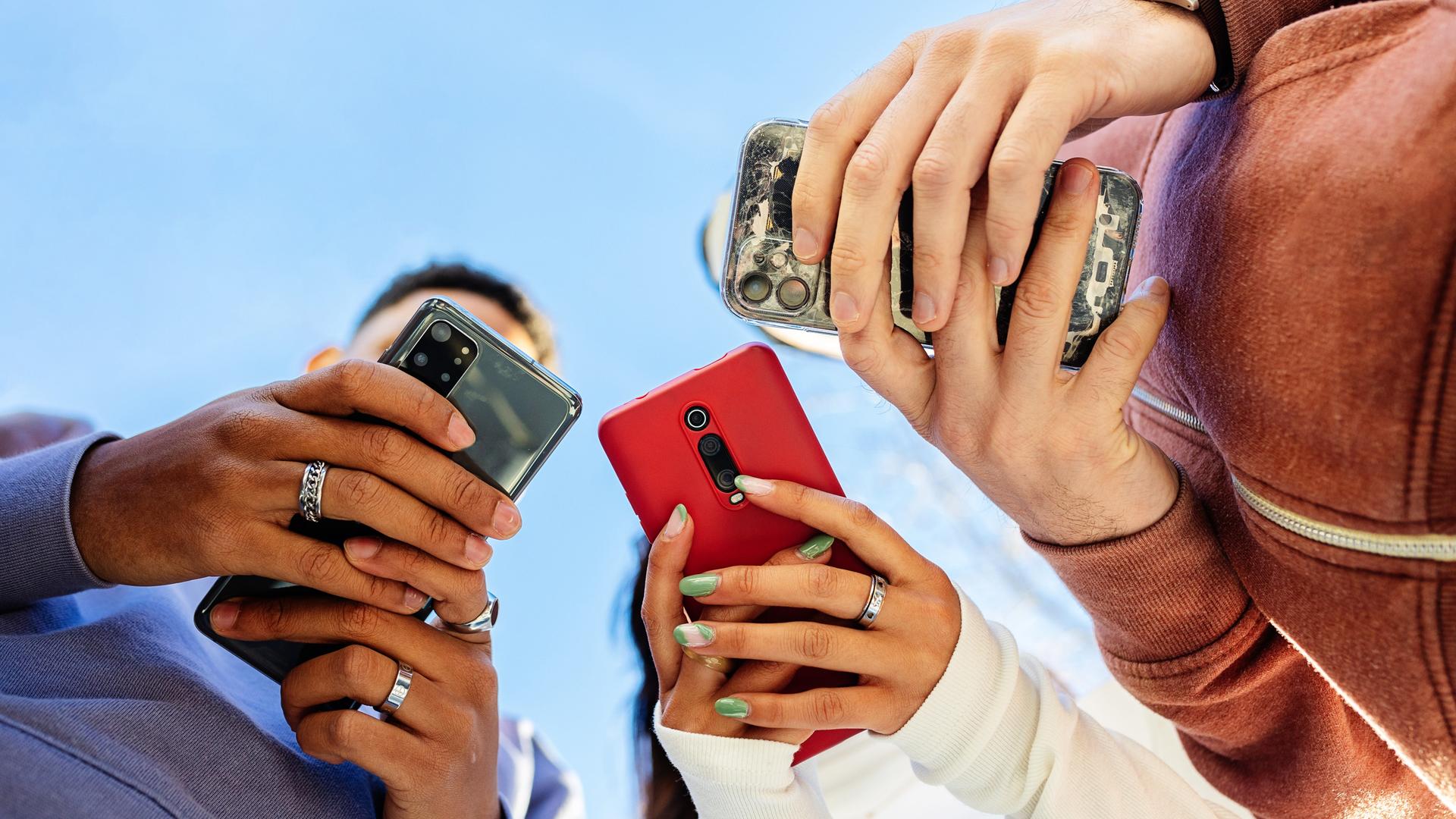 Drei Menschen schauen auf ihre Smartphones, aus der Perspektive von unten betrachtet.