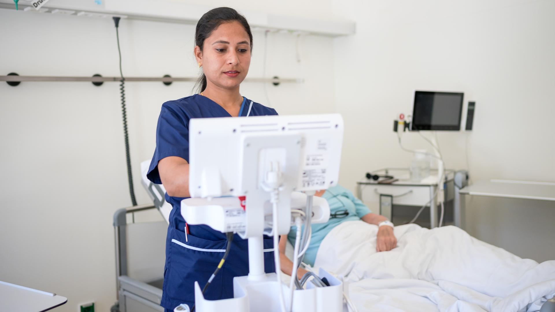 Die Frau steht am Bett eines Patienten und studiert die Krankenakte.