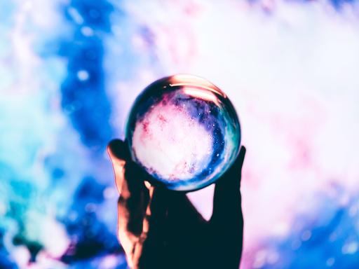 Nahaufnahme einer Hand, die vor blauem Hintergrund eine Glaskugel hält. Nahaufnahme einer Hand, die vor blauem Hintergrund eine Glaskugel hält.