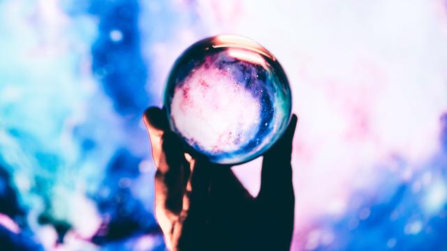 Nahaufnahme einer Hand, die vor blauem Hintergrund eine Glaskugel hält.