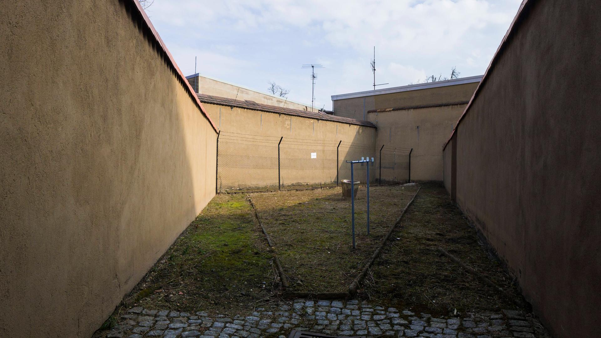 Blick in einen Gefängnishof mit hohen Mauern und etwas Rasen.