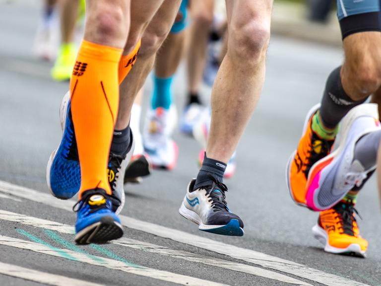 Nahaufnahme von Laufschuhen, Waden und Beinen der Läufer auf einer Strasse.