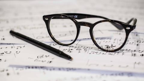 Auf einem unsortierten Stapel von Notenpapier liegt ein Stift und eine Brille.