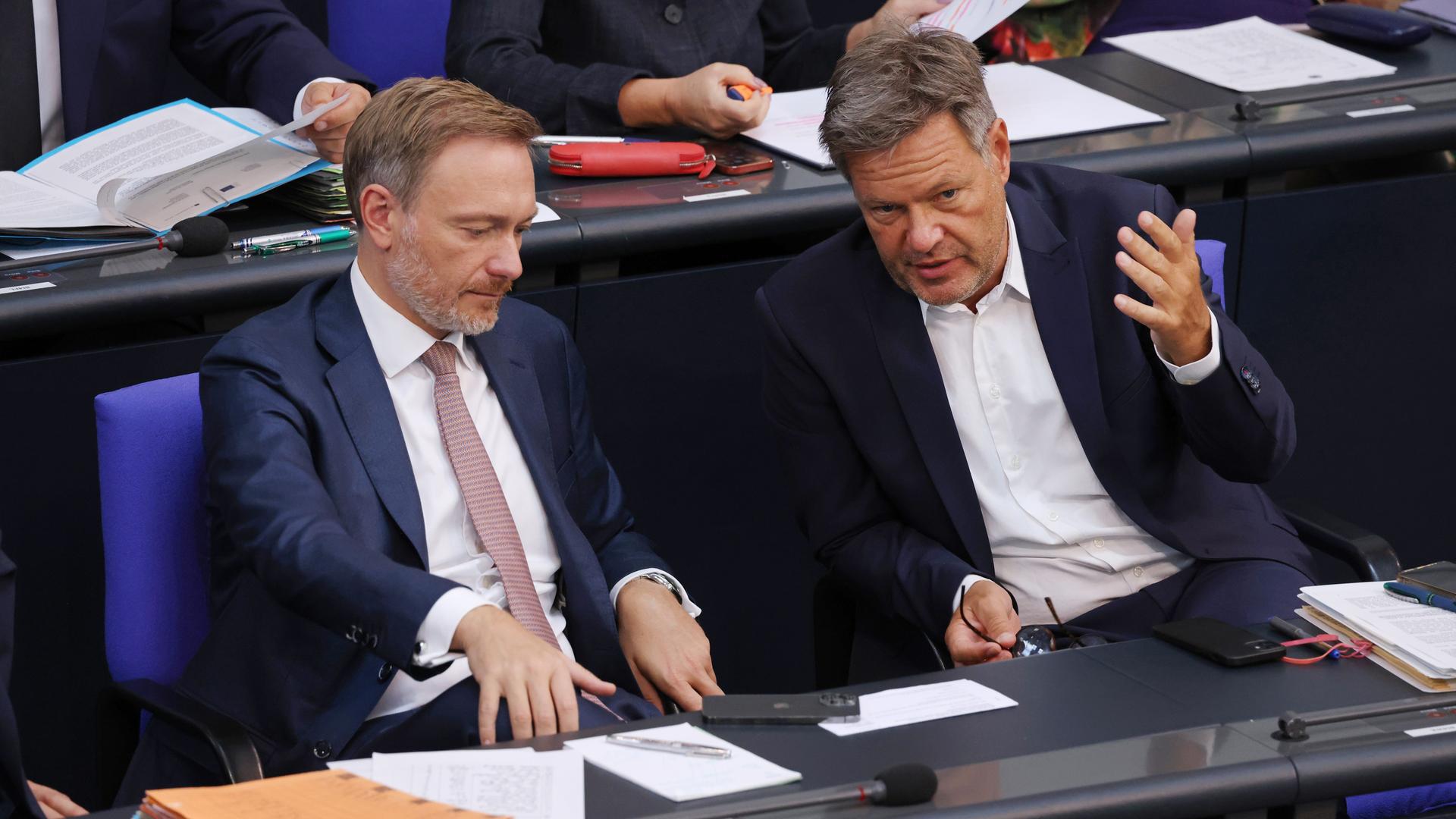 Robert Habeck und Christian Lindner sitzen bei einer Bundestagsdebatte nebeneinander. Habeck redet und gestikuliert mit den Händen, Lindner hört zu. 