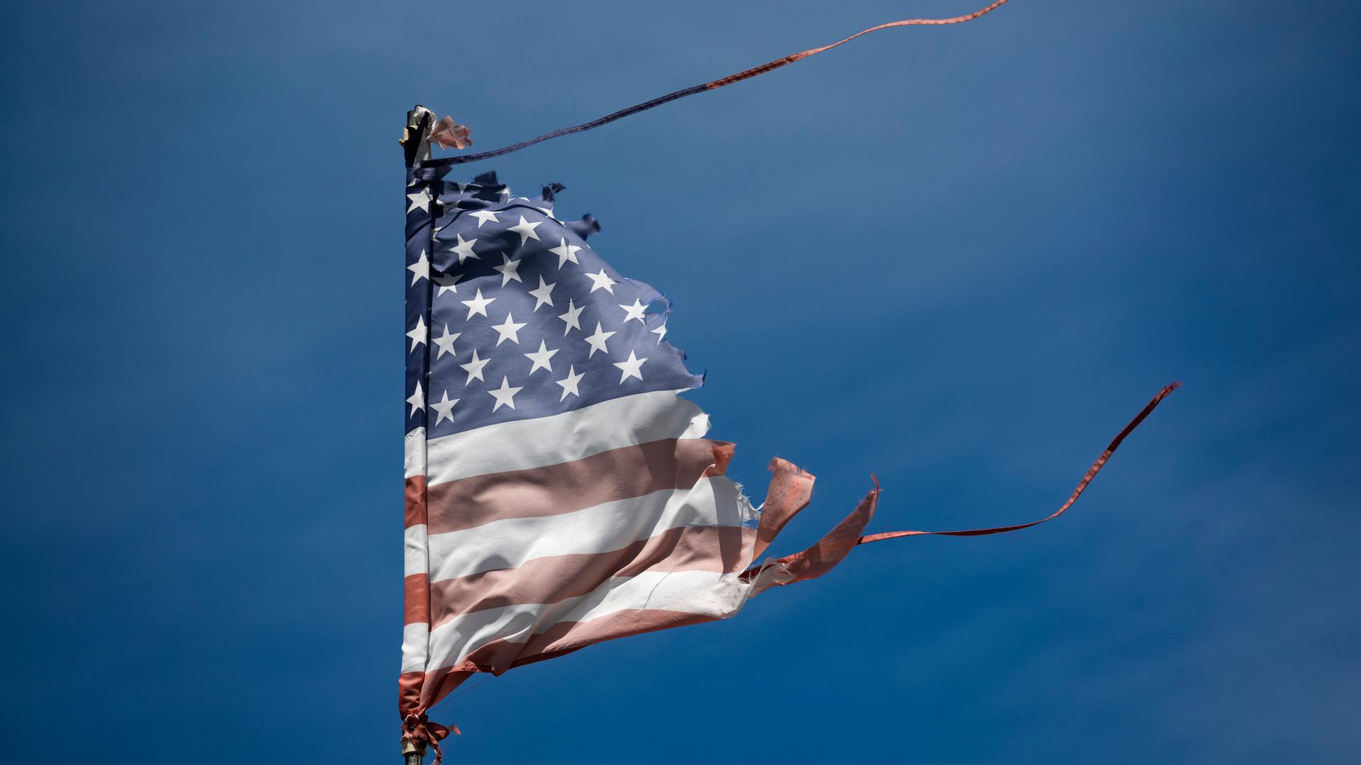 Eine abgenutzte und vom Wind zerzauste amerikanische Flagge weht vor dem blauen Himmel