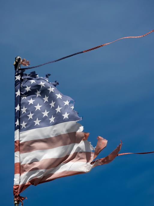 Eine abgenutzte und vom Wind zerzauste amerikanische Flagge weht vor dem blauen Himmel