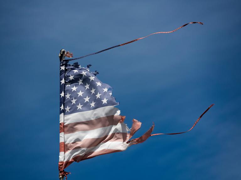 Eine abgenutzte und vom Wind zerzauste amerikanische Flagge weht vor dem blauen Himmel