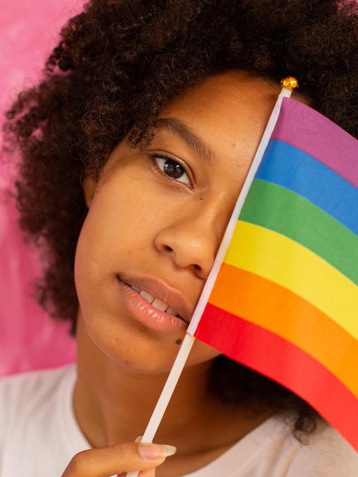 Eine Frau hält sich eine LGBTQI+ Flagge vor das Gesicht