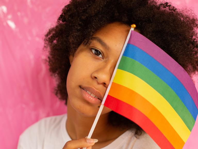 Eine Frau hält sich eine LGBTQI+ Flagge vor das Gesicht