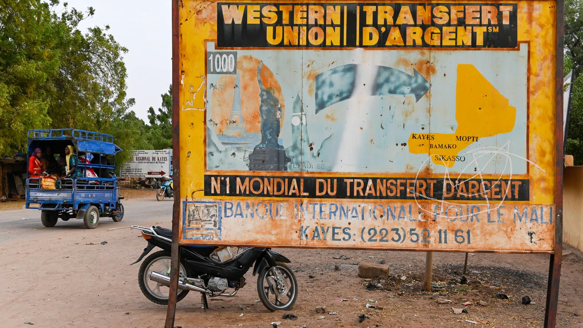 Altes Schild von Western Union in Mali. Es zeigt eine Illustration von Wahrzeichen westlicher Städte, von denen ein Pfeil nach Mali führt.