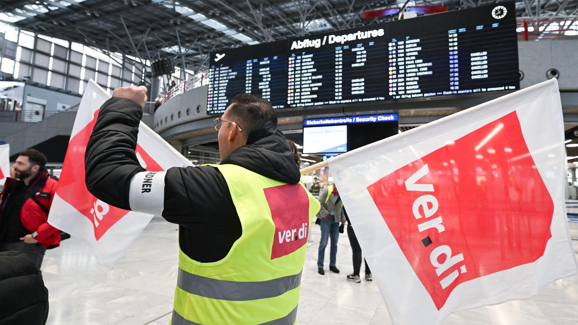 10.03.2025, Baden-Württemberg, Stuttgart: Mitglieder der Gewerkschaft Verdi stehen mit Fahnen bei einem Streik in einem Teminal des Stuttgarter Flughafens.