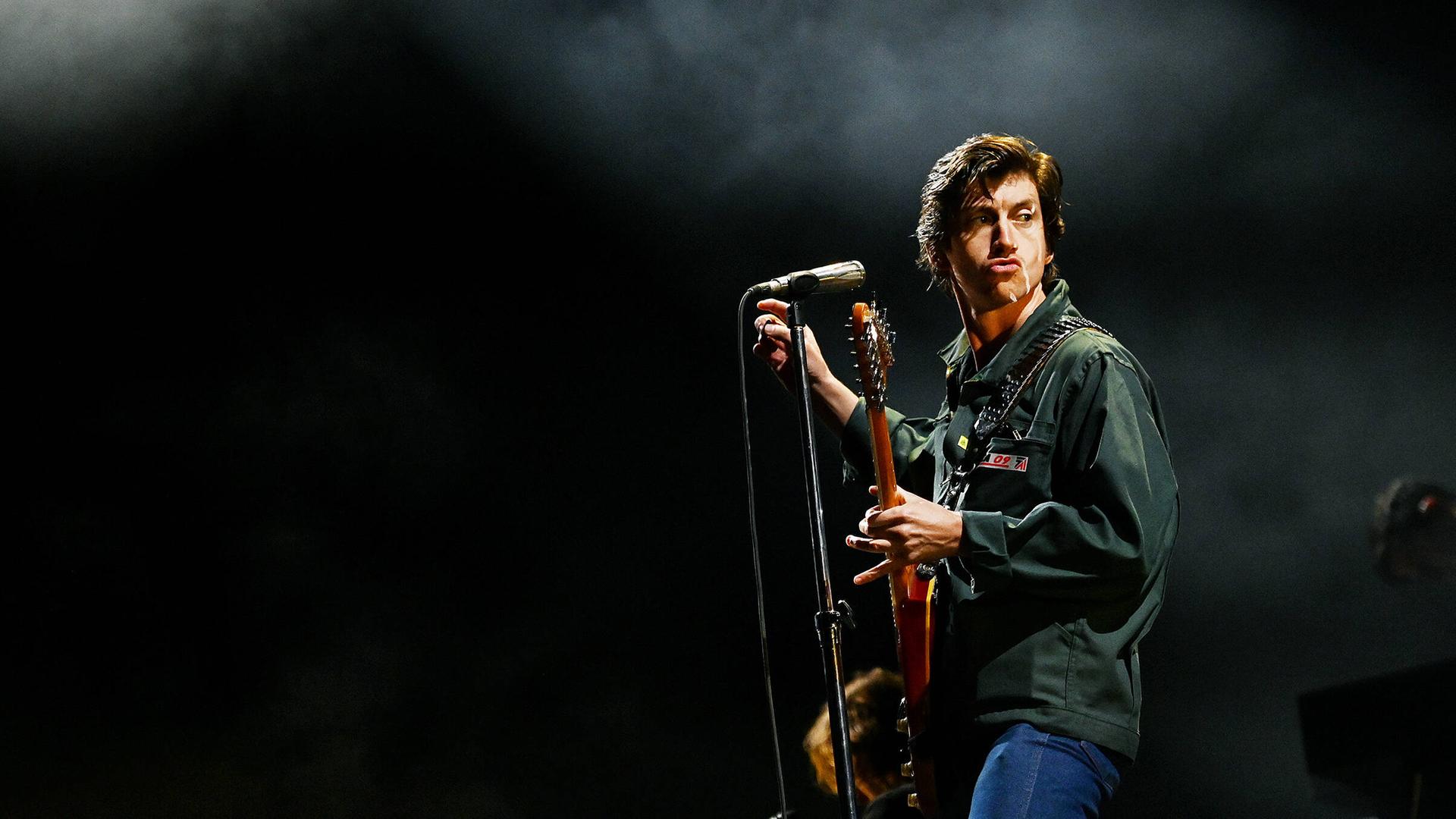 Arctic-Monkeys-Sänger Alex Turner posiert auf der Bühne mit Gitarre und Mikrofon.