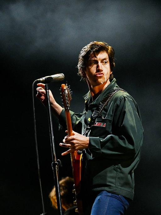 Arctic-Monkeys-Sänger Alex Turner posiert auf der Bühne mit Gitarre und Mikrofon.