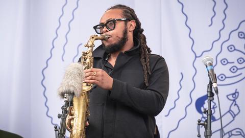 Ein Musiker mit Hornbrille und Dreadlocks spielt Saxophon. 