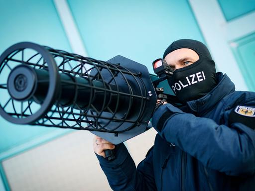 Ein Bundespolizist hält einen schwarze Jammer, eine Waffe zur Drohnenabwehr, auf seiner Schulter.
