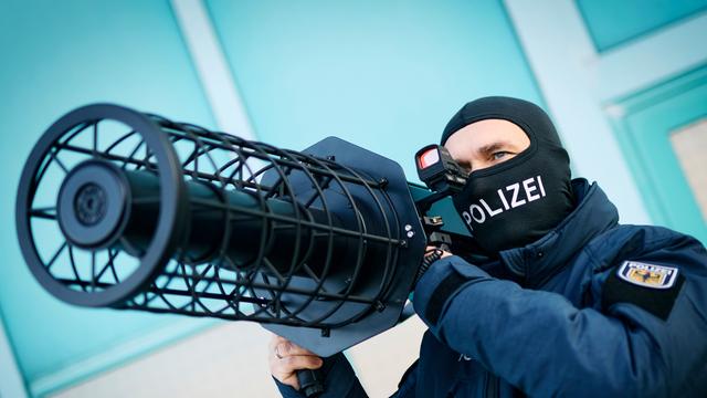 Ein Bundespolizist hält einen schwarze Jammer, eine Waffe zur Drohnenabwehr, auf seiner Schulter.