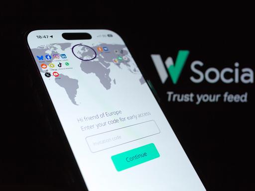 Im Vordergrund ist ein Mobiltelefon auf dem eine Weltkarte abgebildet ist. Darauf ist Europa mit einenm Kreis markiert. Im Hintergrund ist das Logo der Plattform "W Social" 