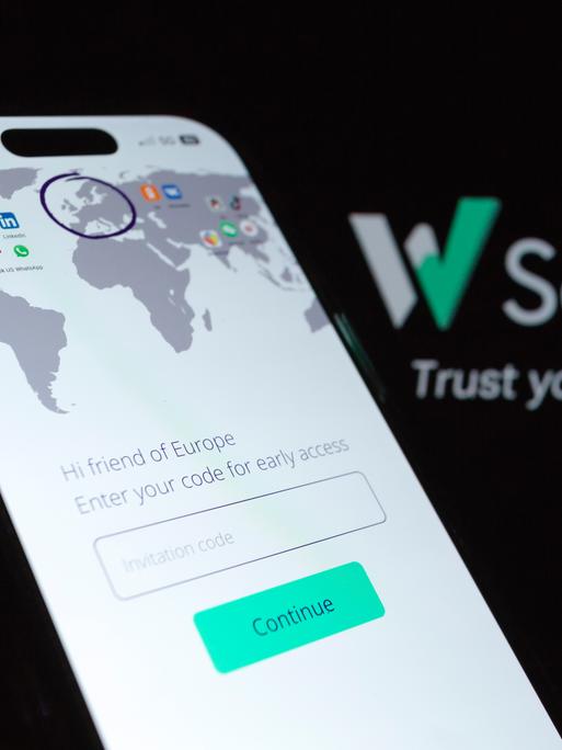 Im Vordergrund ist ein Mobiltelefon auf dem eine Weltkarte abgebildet ist. Darauf ist Europa mit einenm Kreis markiert. Im Hintergrund ist das Logo der Plattform "W Social" 