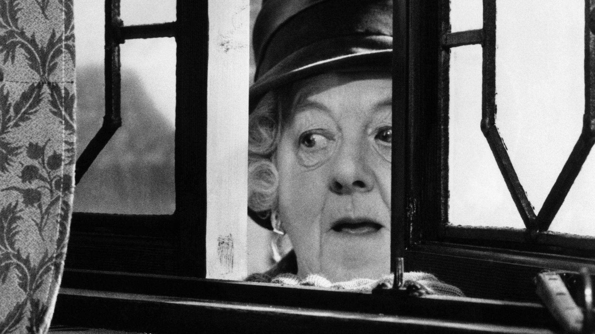 Margaret Rutherford schaut in ihrer Rolle der Miss Marple durch ein leicht geöffnetes Fenster.