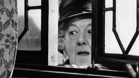 Margaret Rutherford schaut in ihrer Rolle der Miss Marple durch ein leicht geöffnetes Fenster.