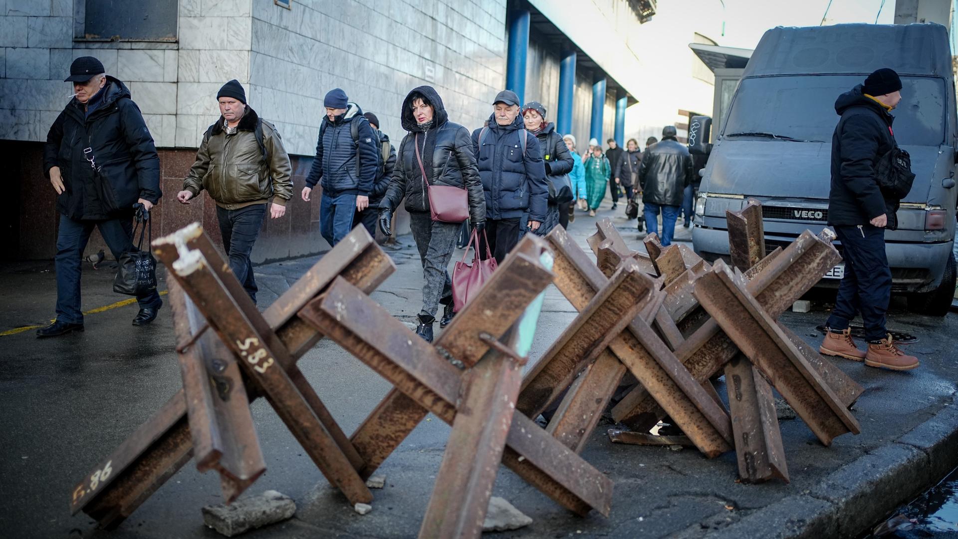 Passanten gehen am Morgen an Panzersperren vor einem Eingang zur Metro in der ukrainischen Hauptstadt Kiew vorbei.