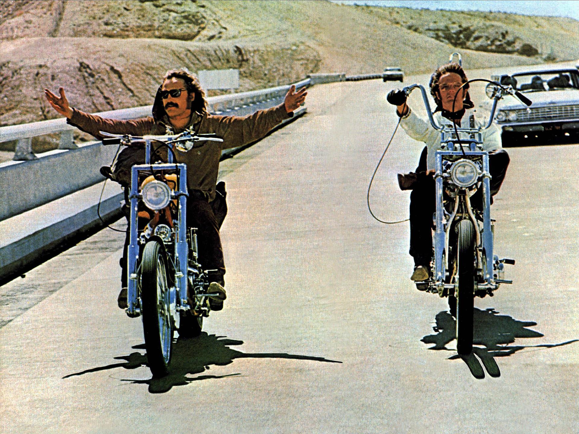 Dennis Hopper und Peter Fonda fahren in einer Filmszene mit Chopper-Motorrädern nebeneinander. Dennis Hopper (l.) fährt freihändig und breitet die Arme aus. 