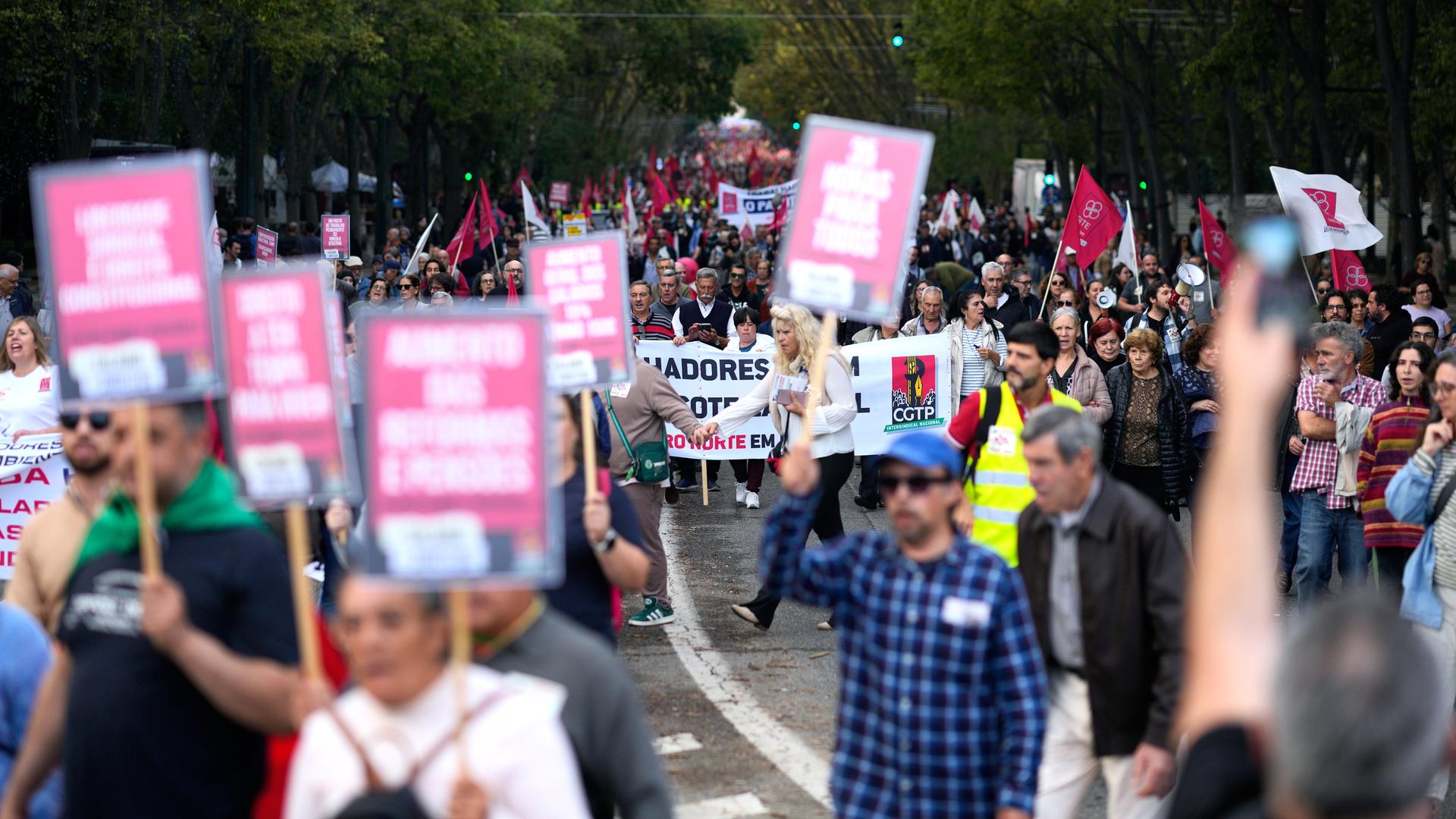 Menschen laufen durch eine Straße und halten Schilder und Transparente mit Protest-Slogans hoch. Menschen laufen durch eine Straße und halten Schilder und Transparente mit Protest-Slogans hoch.
