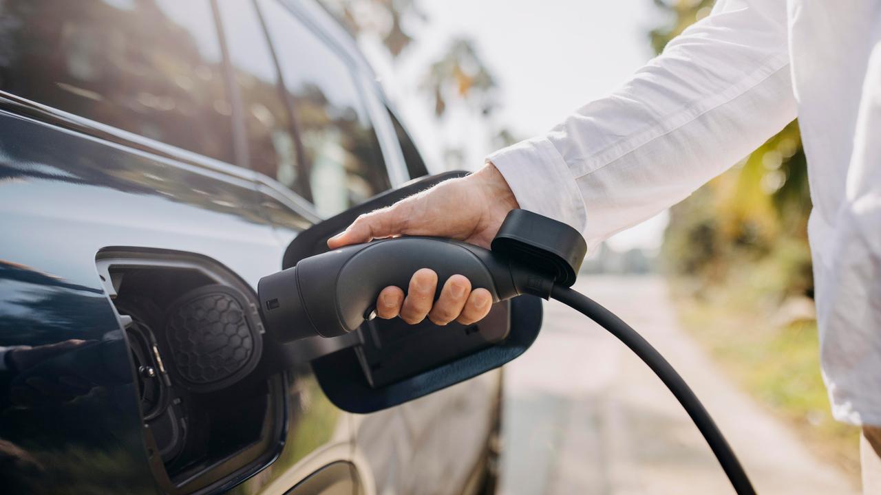 Eine Hand, die ein E-Auto an einer Zapfsäule betankt. 