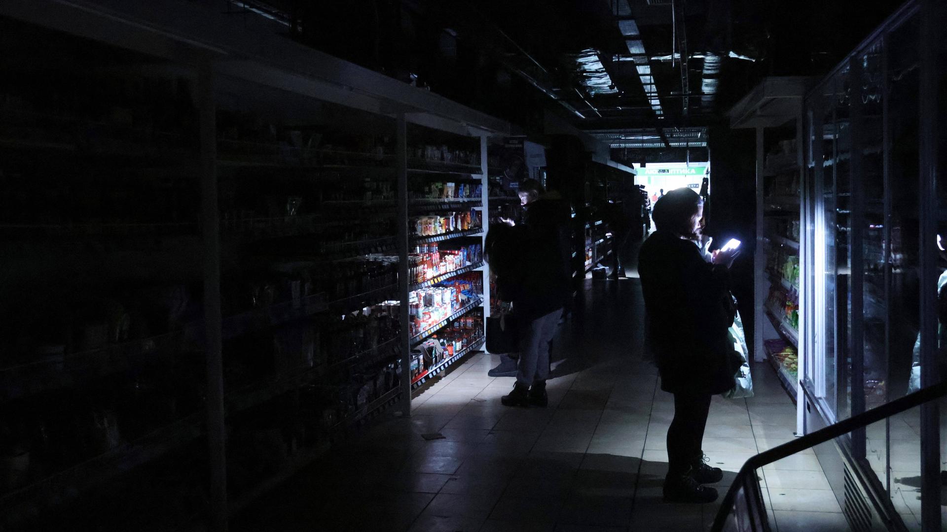 Menschen leuchten in einem Supermarkt mit Taschenlampen in die Regale.