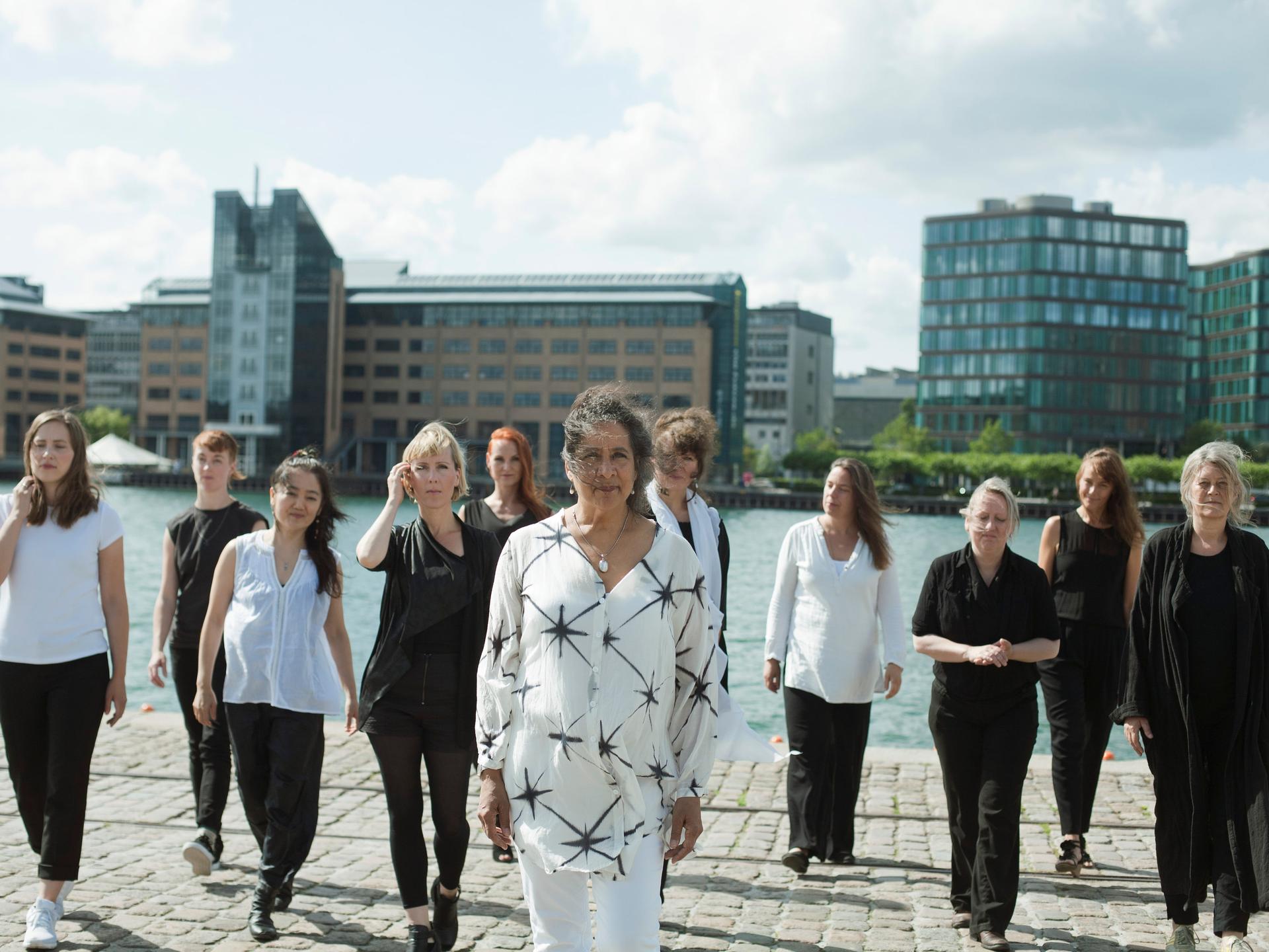 Eine Gruppe von Frauen unterschiedlichen Alters gehen vom Ufer eines städtischen Gewässers auf die Kamera zu.