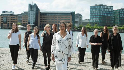 Eine Gruppe von Frauen unterschiedlichen Alters gehen vom Ufer eines städtischen Gewässers auf die Kamera zu.