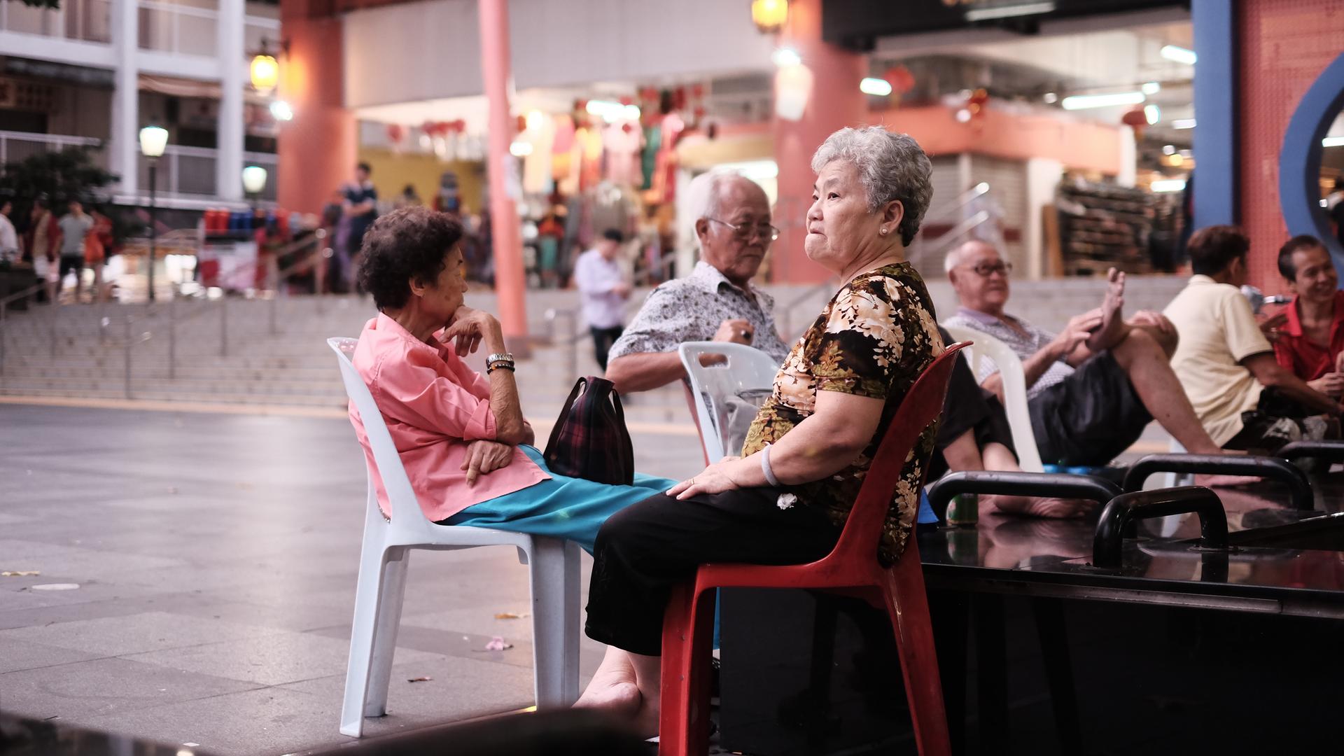 Senioren sitzen auf Plastikstühlen am Eingang eines Tempels in Chinatown, Singapur