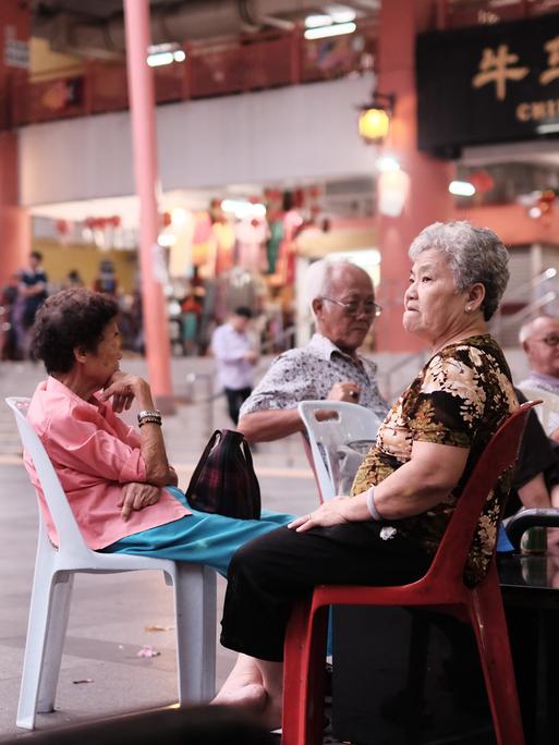 Senioren sitzen auf Plastikstühlen am Eingang eines Tempels in Chinatown, Singapur