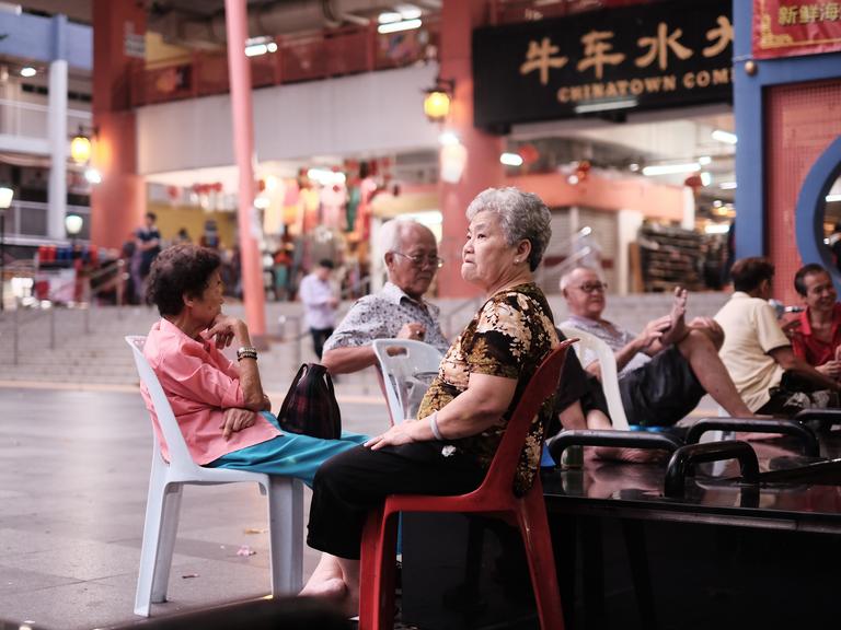 Senioren sitzen auf Plastikstühlen am Eingang eines Tempels in Chinatown, Singapur