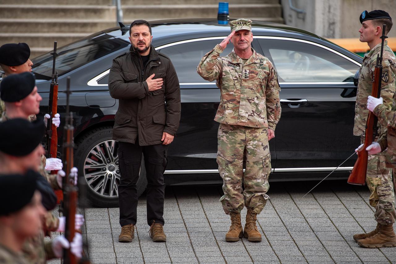 Zwei Männer stehen vor einem Auto und begrüßen Soldaten.