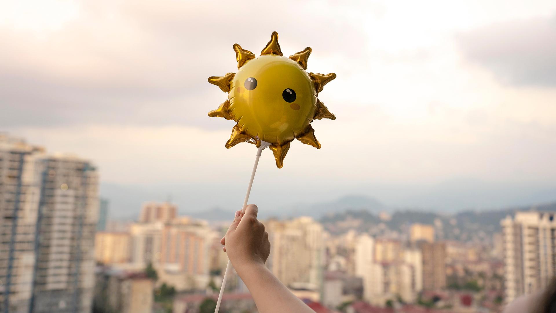 Eine Kinderhand hält einen Sonnenluftballon.