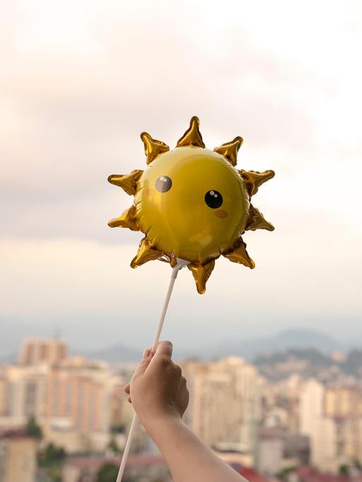 Eine Kinderhand hält einen Sonnenluftballon.