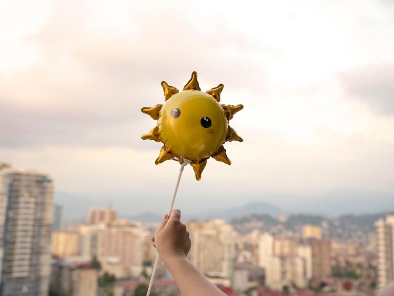 Eine Kinderhand hält einen Sonnenluftballon.