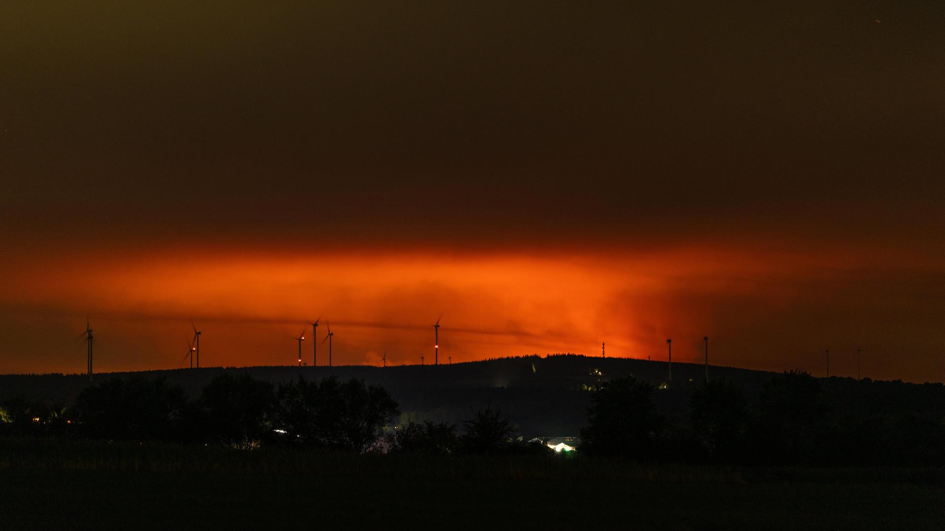 Nachtaufnahme: Am Horizont erhellt rötlicher Flammenschein den Brandrauch des Großbrands im Hohen Venn.