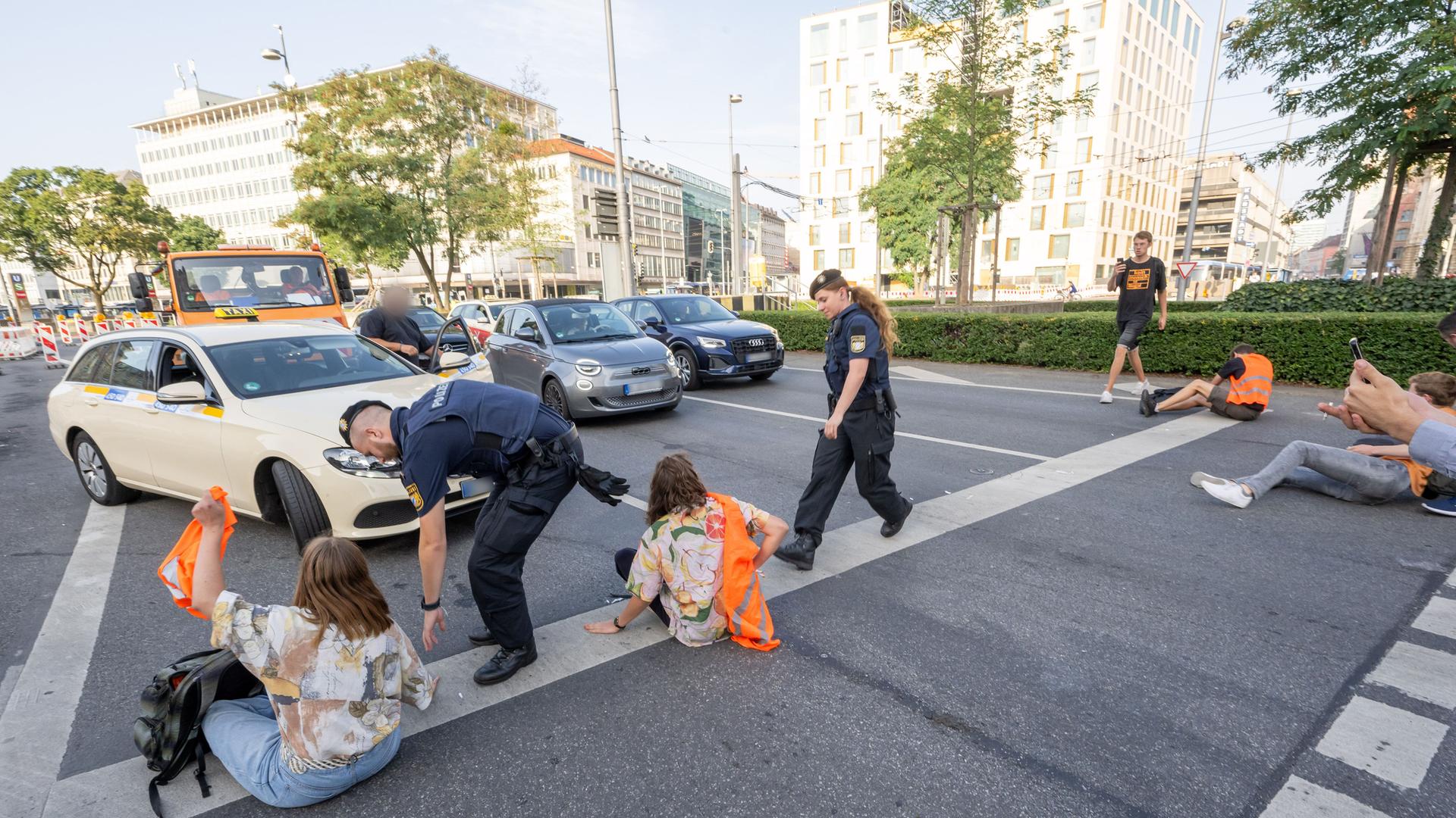 München: Polizisten gehen auf der Kreuzung am Stachus in der Innenstadt zu Teilnehmern" der Letzten Generation", die sich zuvor auf der Strasse festgeklebt haben. Davor stehen wartende Autos. München: Polizisten gehen auf der Kreuzung am Stachus in der Innenstadt zu Teilnehmern" der Letzten Generation", die sich zuvor auf der Strasse festgeklebt haben. Davor stehen wartende Autos.