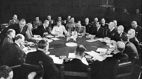 Historisches Schwarzweißfoto von Männer, die bei der Potsdamer Konferenz um einen runden Tisch herum sitzen.