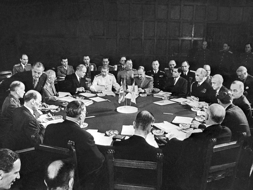 Historisches Schwarzweißfoto von Männer, die bei der Potsdamer Konferenz um einen runden Tisch herum sitzen.
